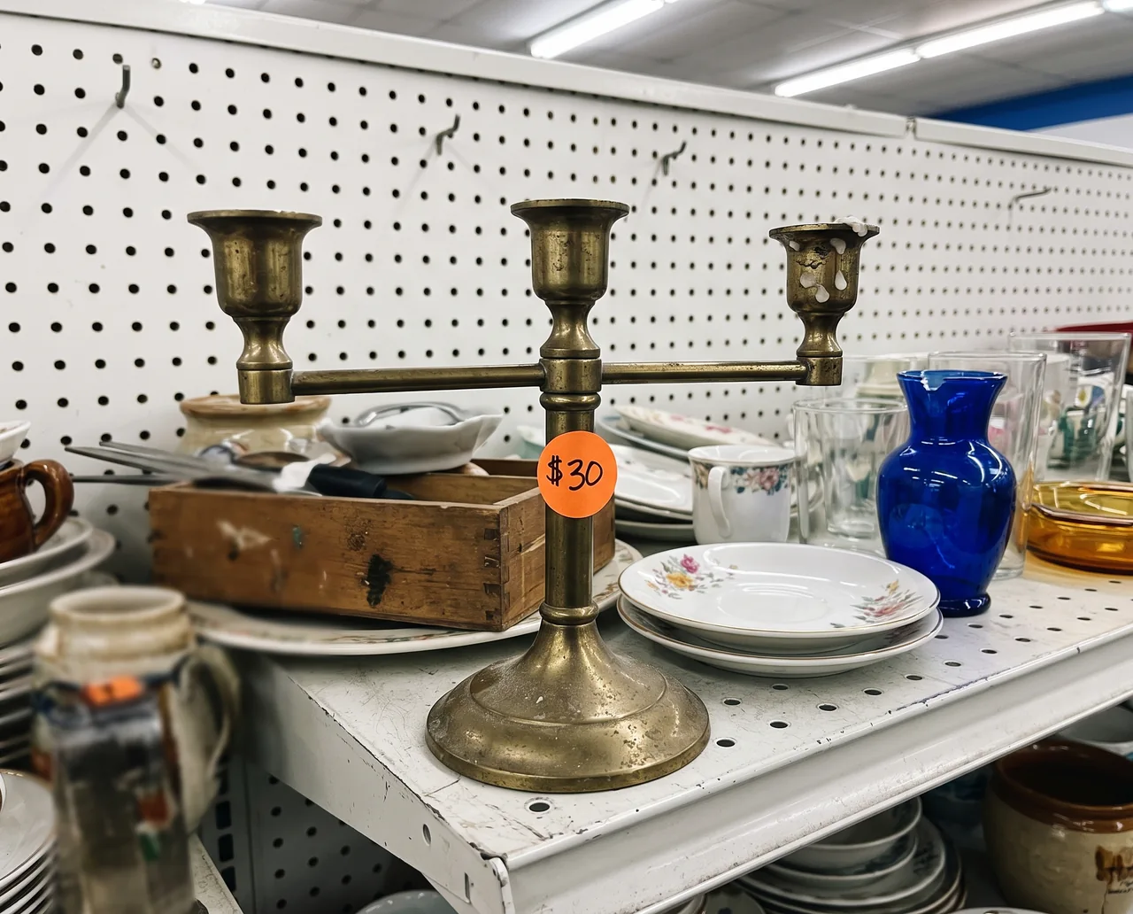 Tarnished brass candelabra with a $30 sticker on a cluttered thrift store shelf